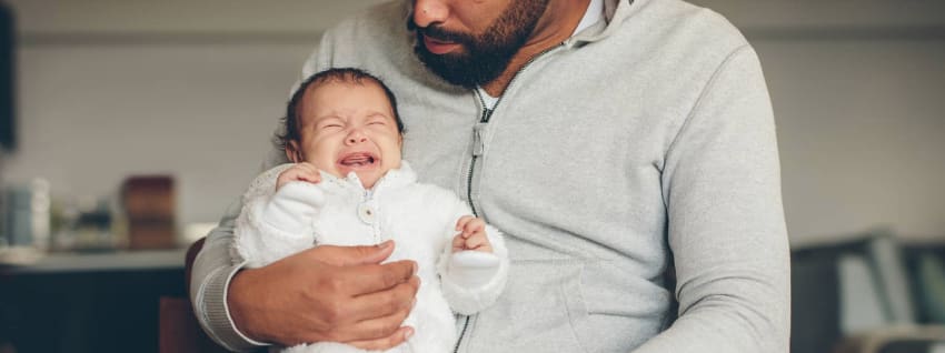 Crying baby upright in dads arms