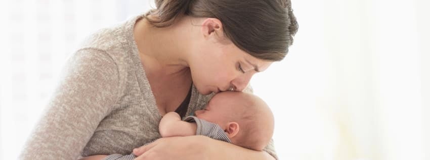 woman comforting and kissing a newborn on the forehead