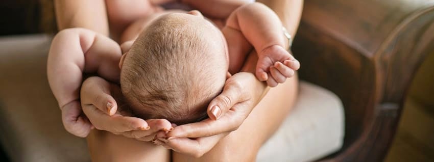 Mother cradling the head of a baby lying on her lap