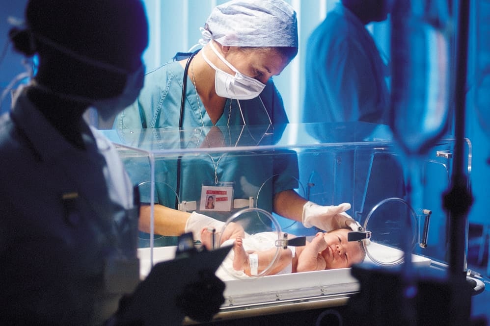 Medical professionals with preterm baby in incubator